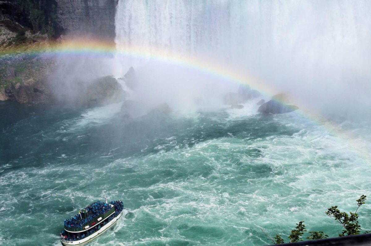 A Maid of the Mist boat in blue ponchos approaching the falls under a rainbow in the spray