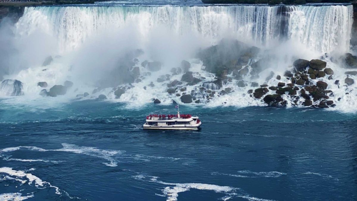 A red-poncho Niagara City Cruises boat on the Niagara River below the American Falls, seen from the Canadian side