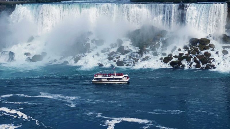A red-poncho Niagara City Cruises boat on the Niagara River below the American Falls, seen from the Canadian side