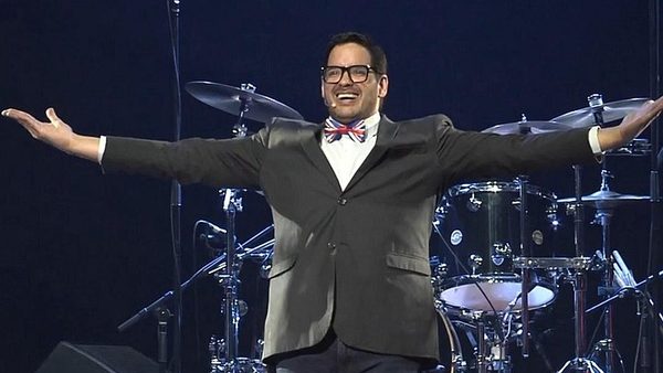 A performer in a bow tie with arms outstretched in front of the drum kit on the Canadiana stage