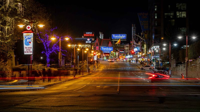 Clifton Hill lit up at night, neon signs and traffic trails along the street