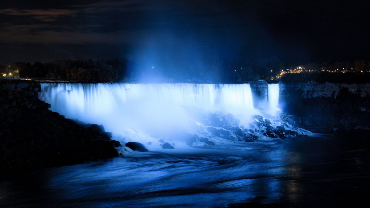 The American Falls floodlit blue after dark, seen from the Canadian side of the Niagara Gorge