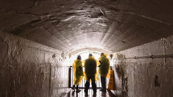 Visitors in yellow ponchos silhouetted in a lit tunnel at Journey Behind the Falls