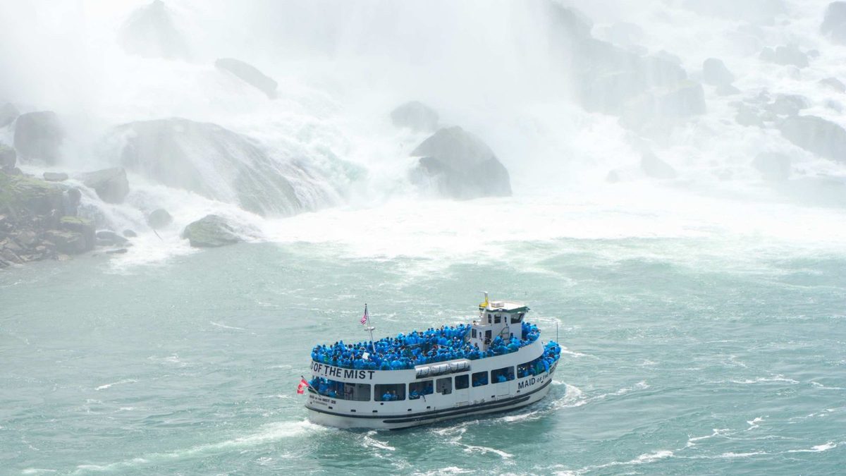 A Maid of the Mist boat crowded with blue ponchos pushing into the spray at the foot of Niagara Falls