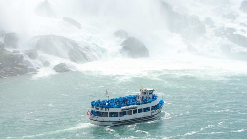 A Maid of the Mist boat crowded with blue ponchos pushing into the spray at the foot of Niagara Falls