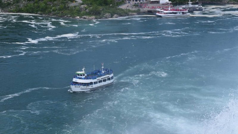 A blue-poncho Maid of the Mist boat on the Niagara River with a red-poncho Niagara City Cruises boat at the Canadian dock behind it