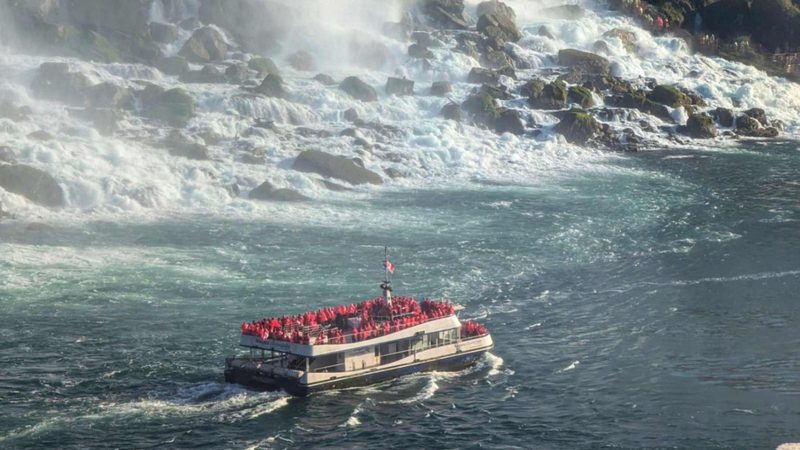 A Niagara City Cruises boat carrying red ponchos across the river below the falls