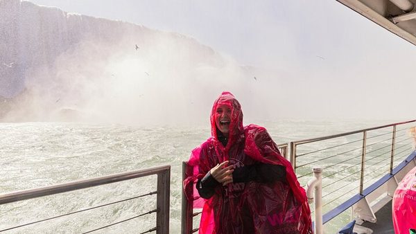 A guest in a red poncho on the deck of a Niagara City Cruises boat in the spray below the falls