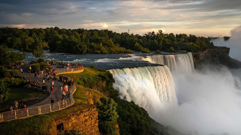 The American Falls and Bridal Veil Falls at sunset, with visitors lining the Prospect Point promenade on the New York side