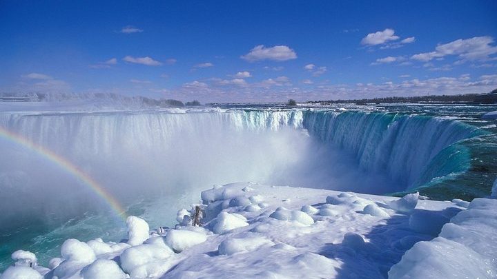 The Horseshoe Falls in winter from the Canadian bank, ice mounds at the base and a rainbow in the spray