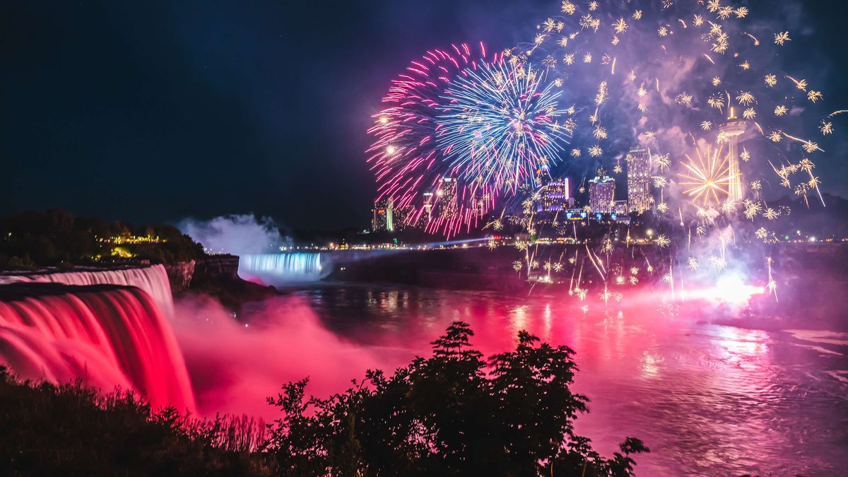 Fireworks bursting over the illuminated Niagara Falls at night