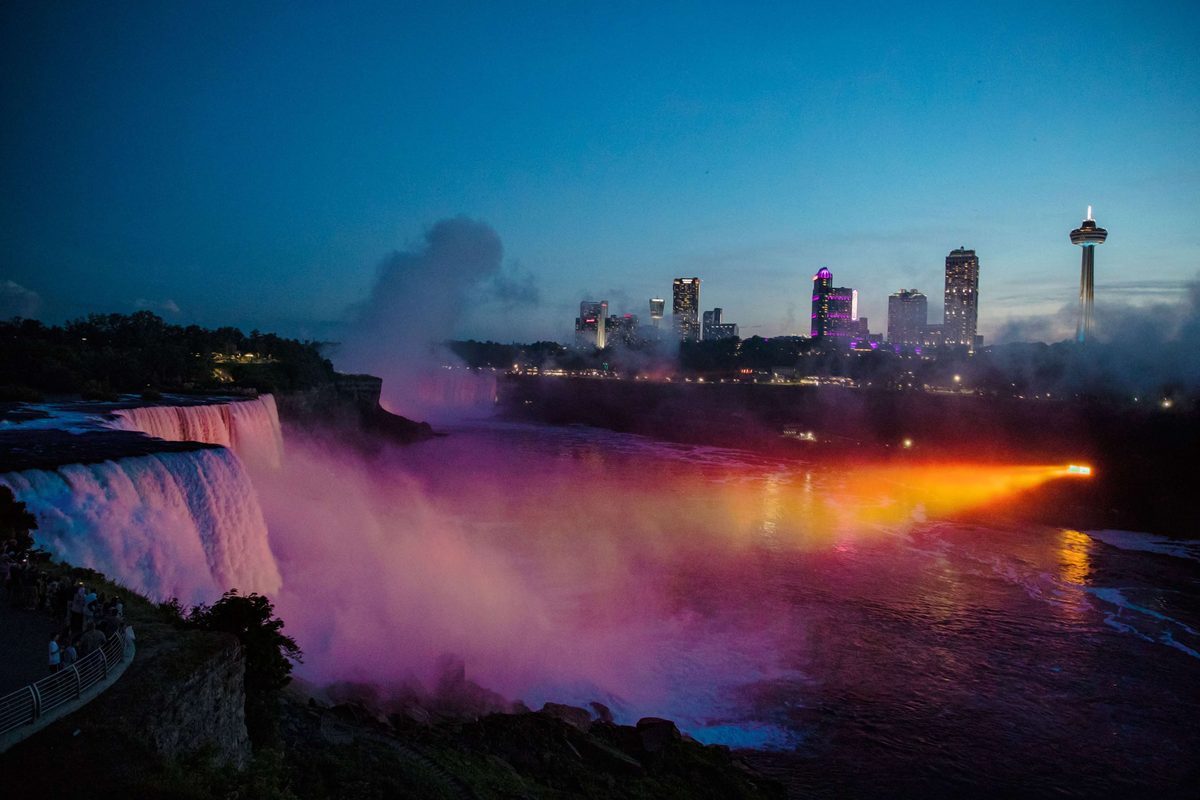 Coloured light in the mist above the falls, with the city skyline behind