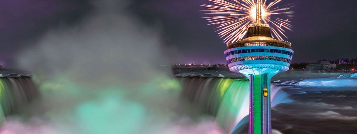 A firework bursting above the floodlit Skylon Tower with the illuminated Horseshoe Falls behind