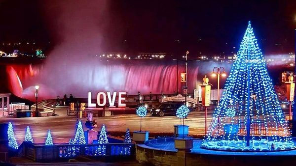 A lit blue Christmas tree beside the Horseshoe Falls illuminated pink at night