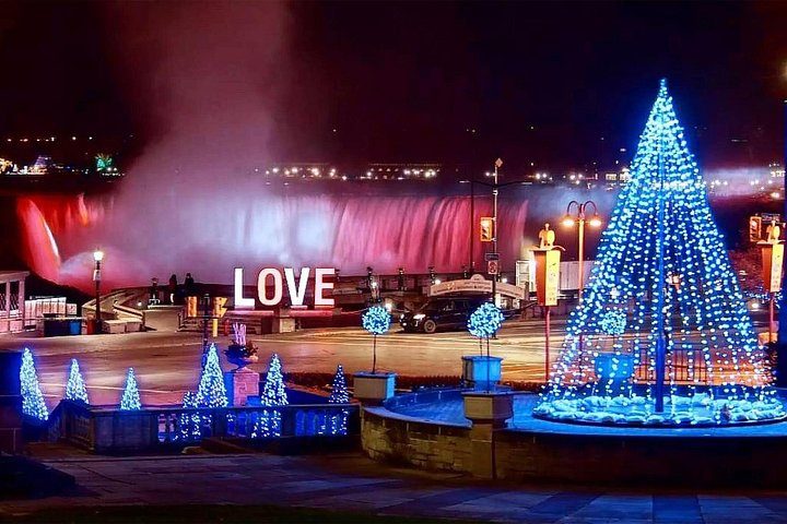 A lit Christmas tree and illuminated LOVE sign in Queen Victoria Park, with the falls floodlit red behind