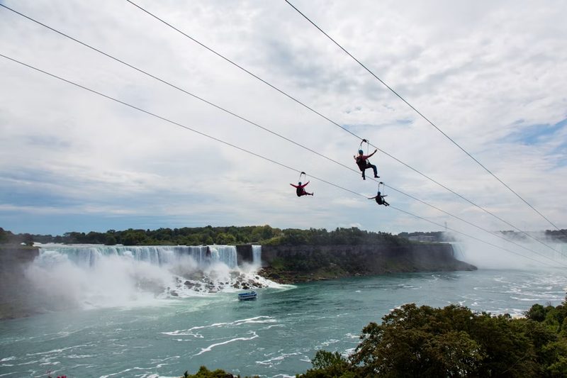 Three riders on the WildPlay zipline in mid flight with the American Falls behind